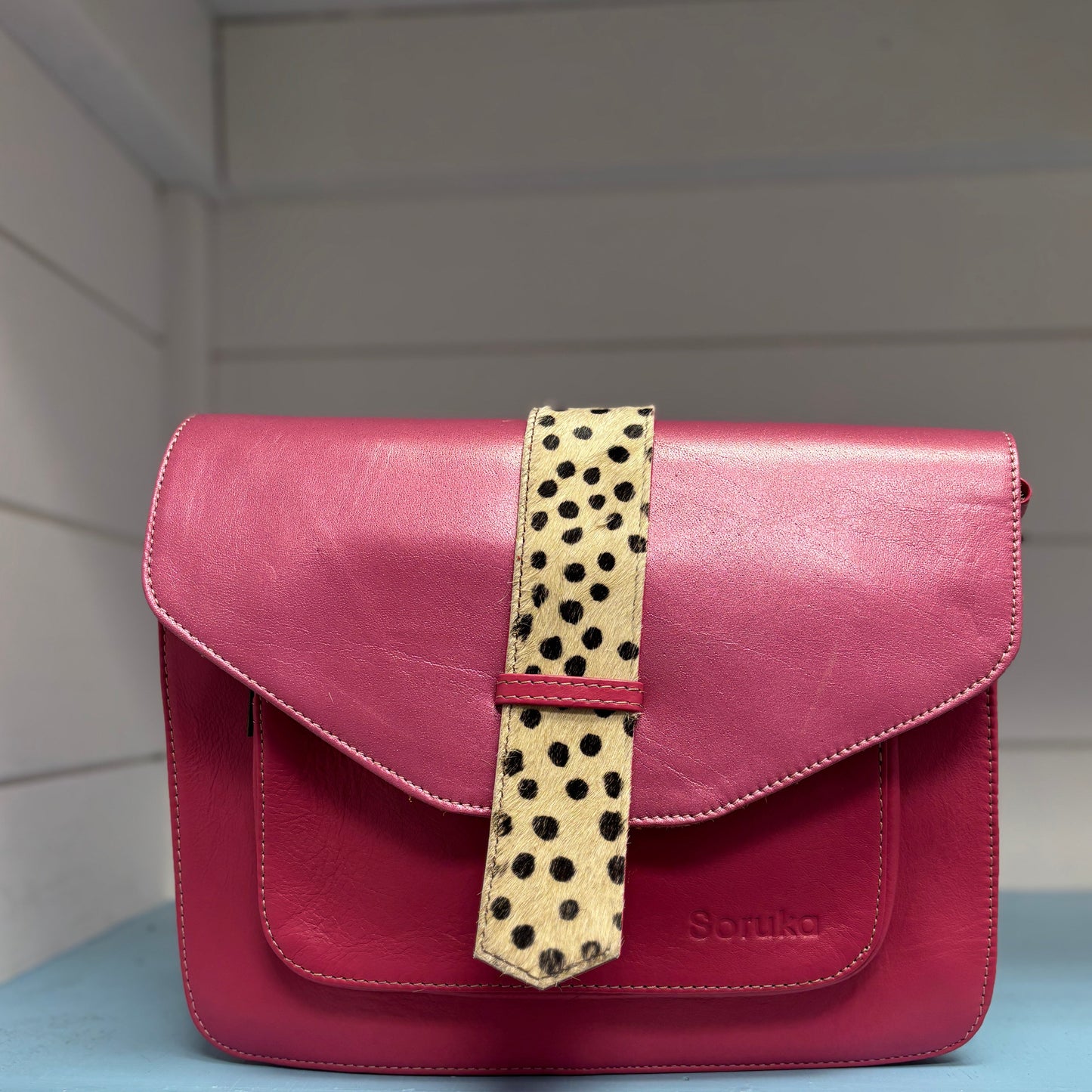 Pink handbag with a leopard print strap on a shelf
