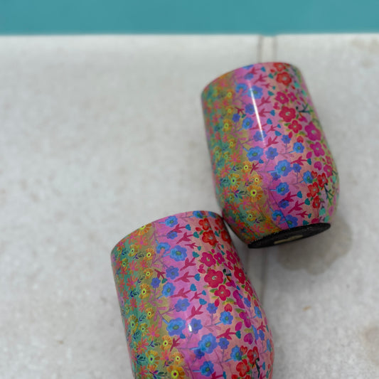 Two colorful floral-patterned cylindrical objects on a white surface with a blue background