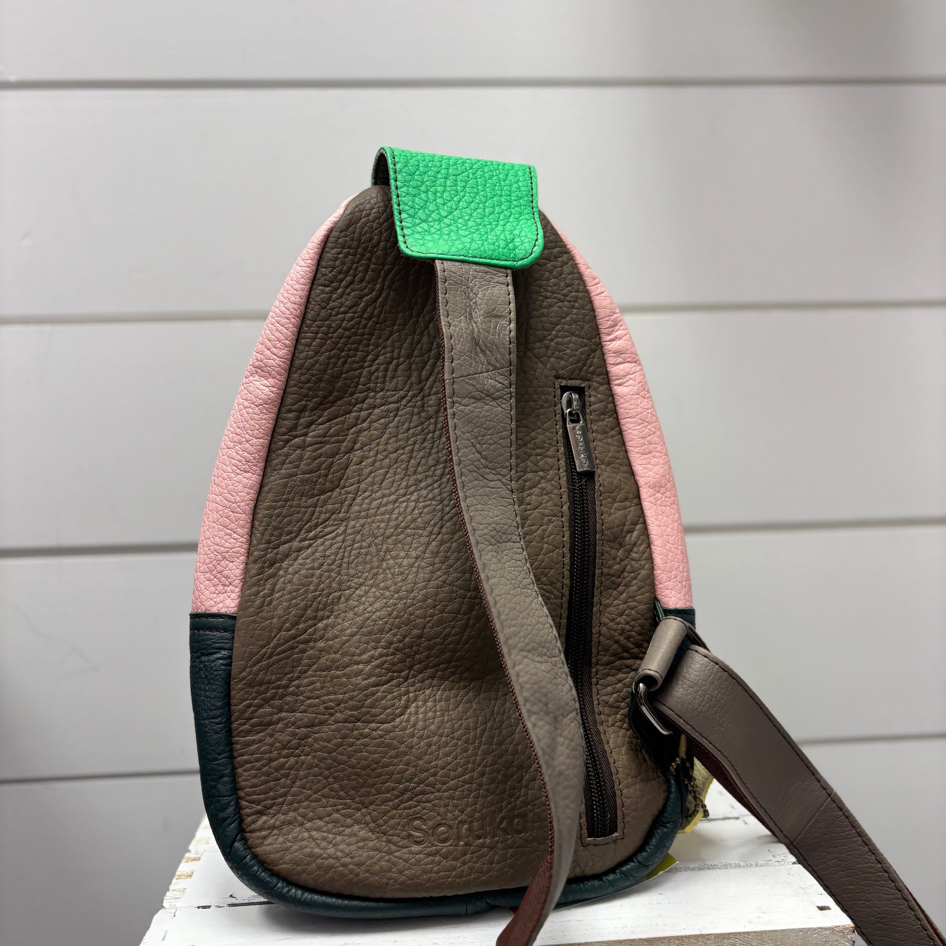 Brown leather bag with pink interior and green flap on a white surface against a gray background