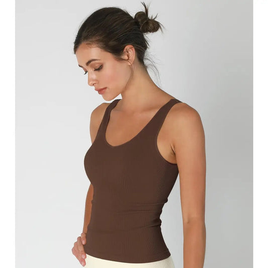 Woman wearing a brown tank top and white pants on a gray background